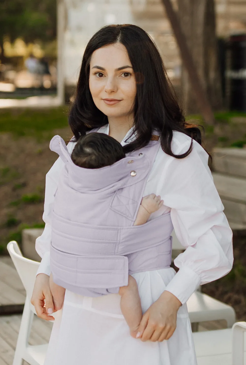 Mutter mit Baby in der marsupi breeze Babytrage in Lilac sitzt am Tisch und spricht mit Partner
