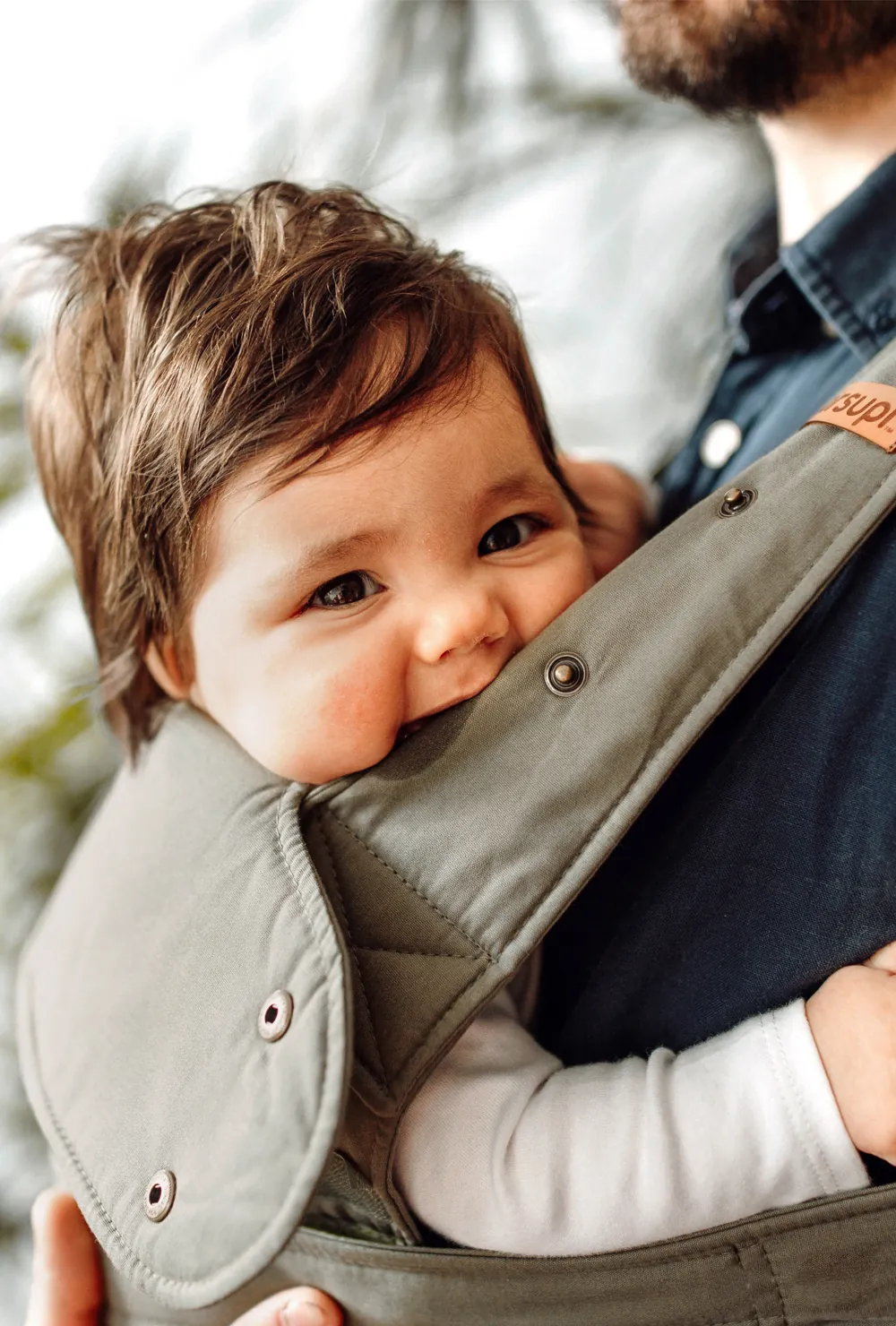 Nahaufnahme: Baby in der Marsupi Classic 2 Babytrage Olivgrün (Olive) kuschelt und schaut in die Kamera