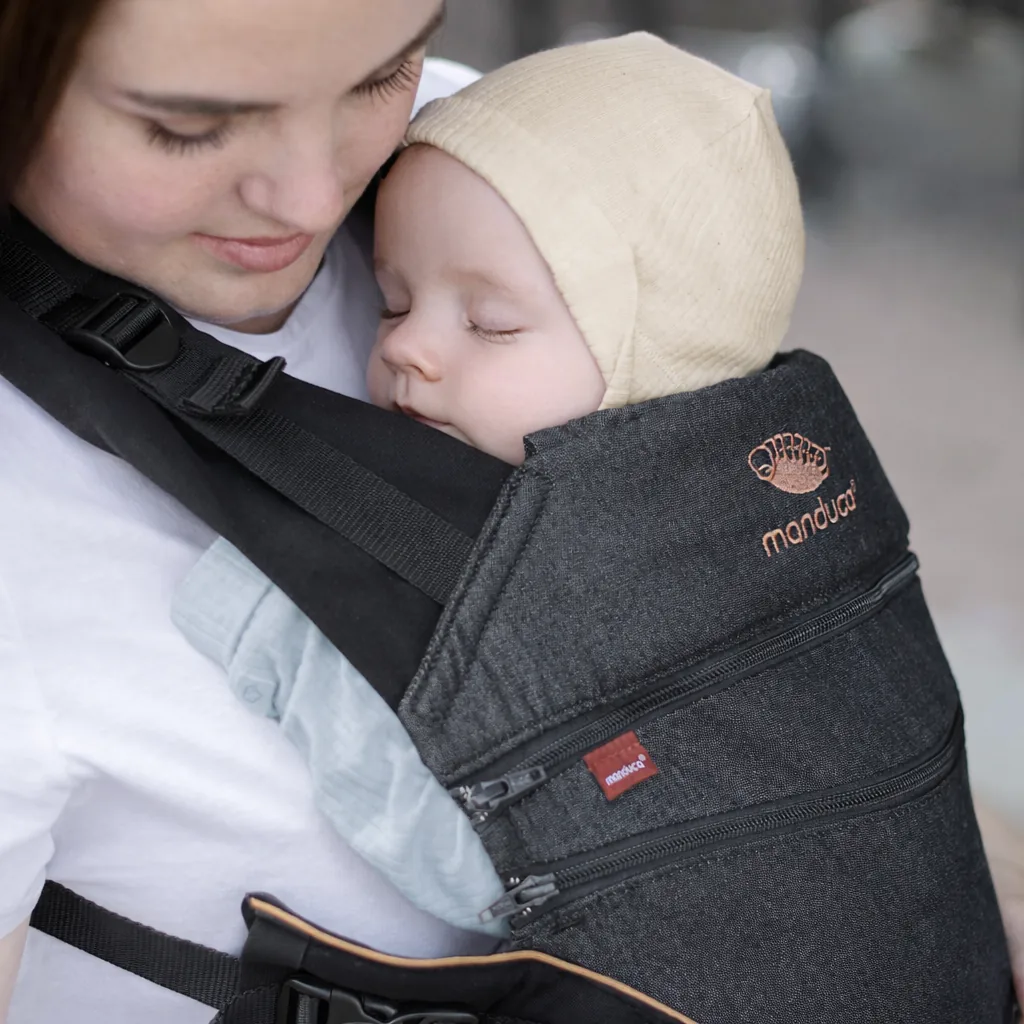 Nahaufnahme eines Neugeborenen, das friedlich in einer manduca® Babytrage auf der Brust eines Elternteils schläft