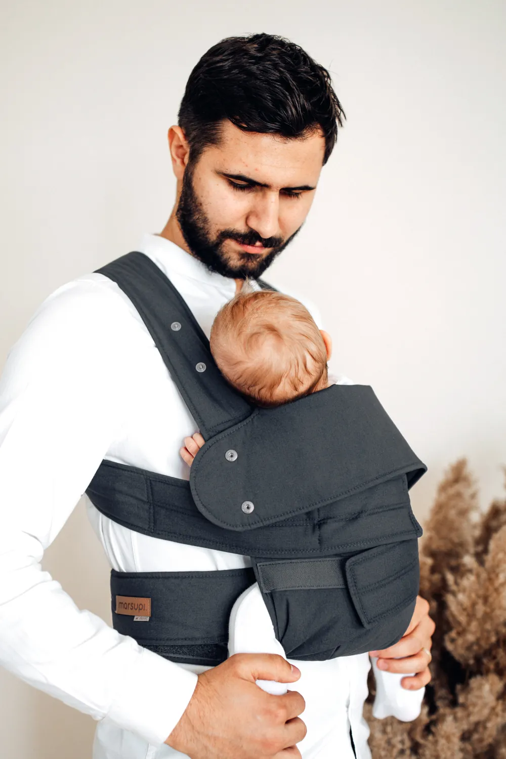 Vater trägt ein Baby in der Marsupi Classic 2 Babytrage in Grau – Lifestylefoto mit hellem Hintergrund.